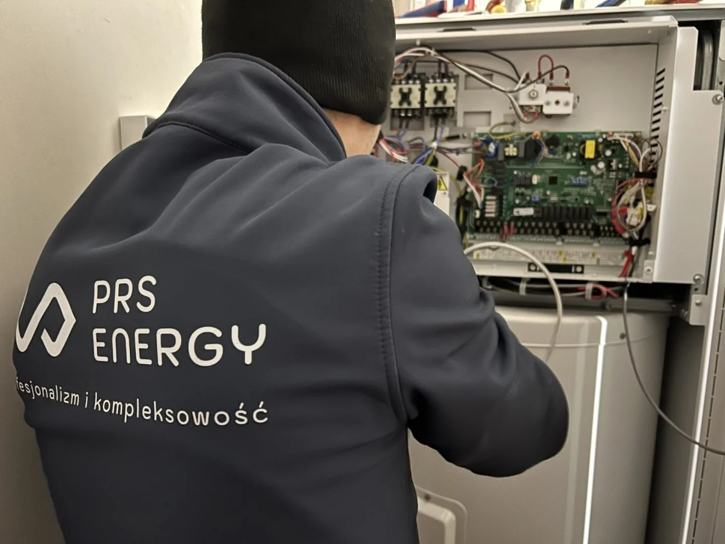 Technik serwisuje otwartą szafę sterowniczą z układem elektronicznym.